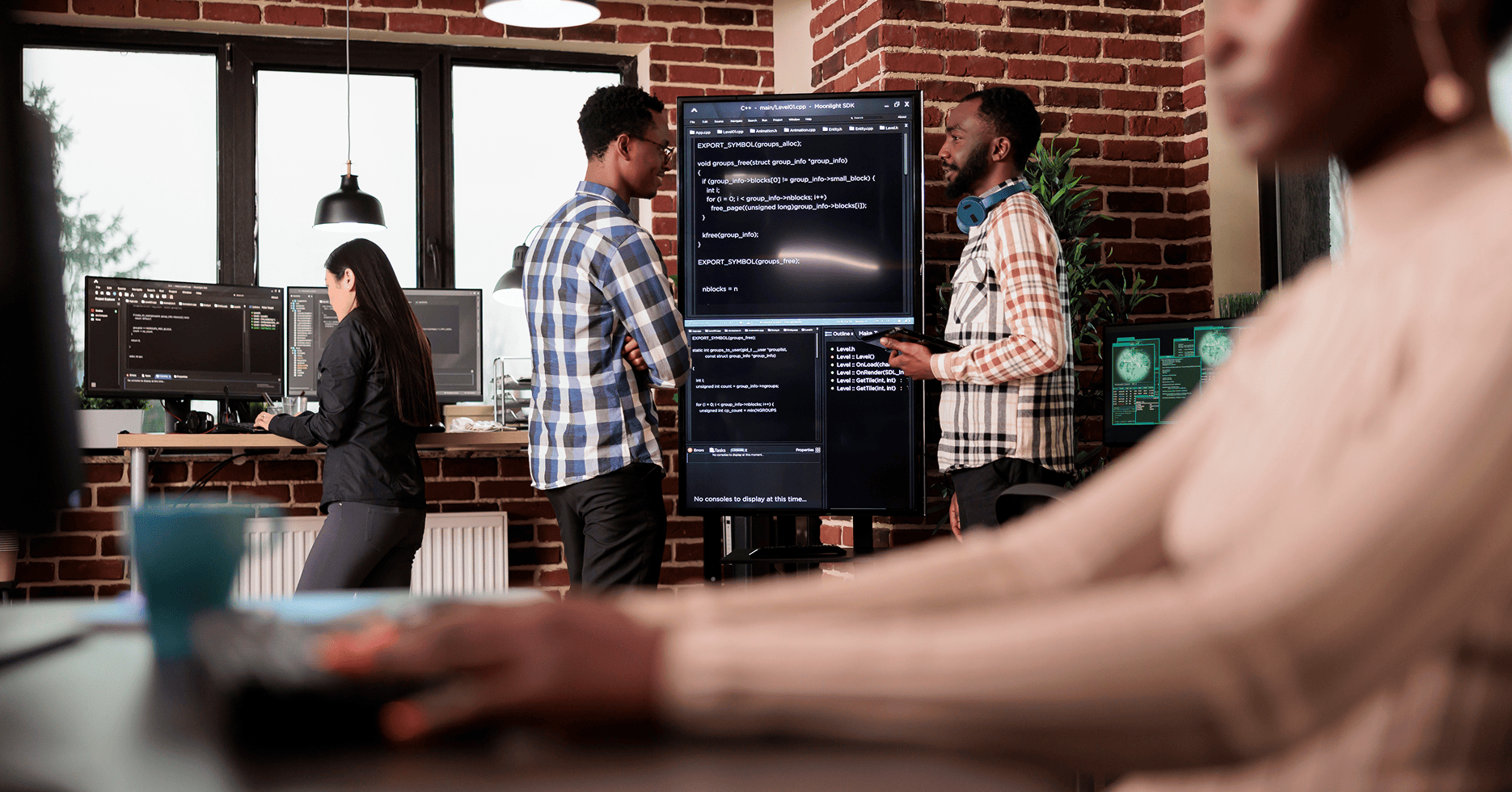 Software engineers reviewing code on a large monitor in a collaborative tech office, working through the challenges of taking an AI pilot to production.
